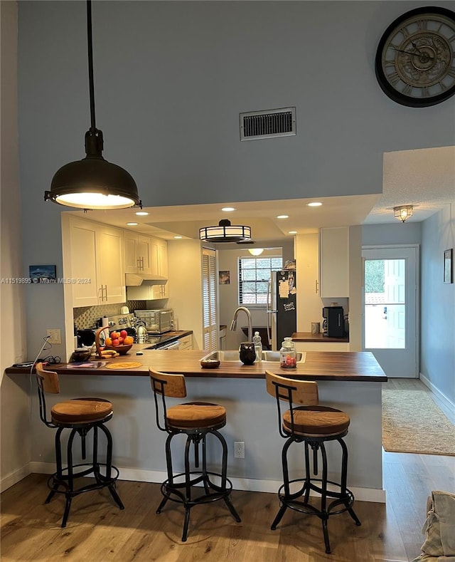 kitchen featuring a healthy amount of sunlight, kitchen peninsula, white cabinetry, and wood-type flooring