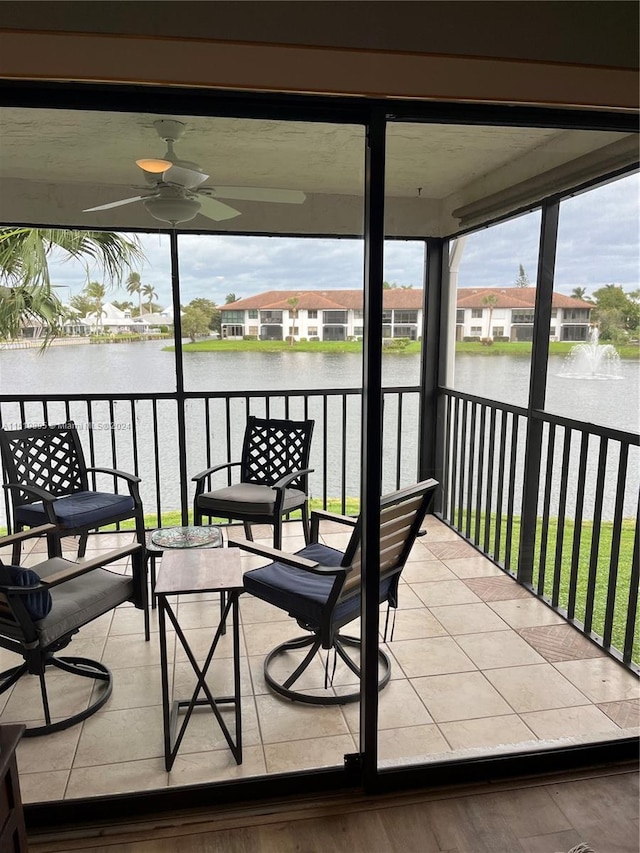 sunroom with ceiling fan and a water view