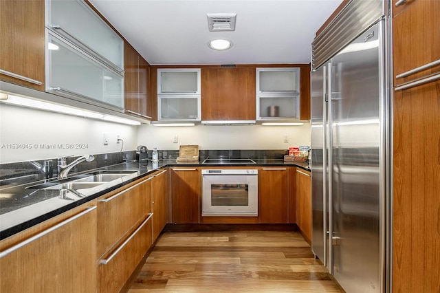 kitchen featuring sink, wood-type flooring, black stovetop, stainless steel built in fridge, and oven