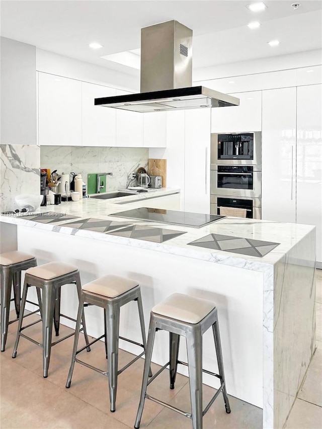 kitchen with a breakfast bar, kitchen peninsula, white cabinetry, and island exhaust hood