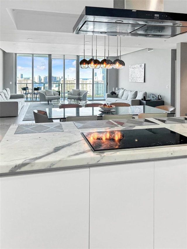 kitchen with light stone countertops, a wealth of natural light, exhaust hood, and decorative light fixtures