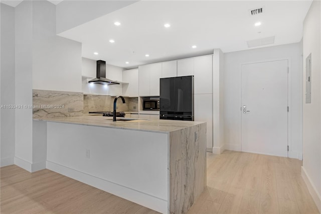 kitchen with light hardwood / wood-style floors, wall chimney range hood, tasteful backsplash, black appliances, and white cabinetry