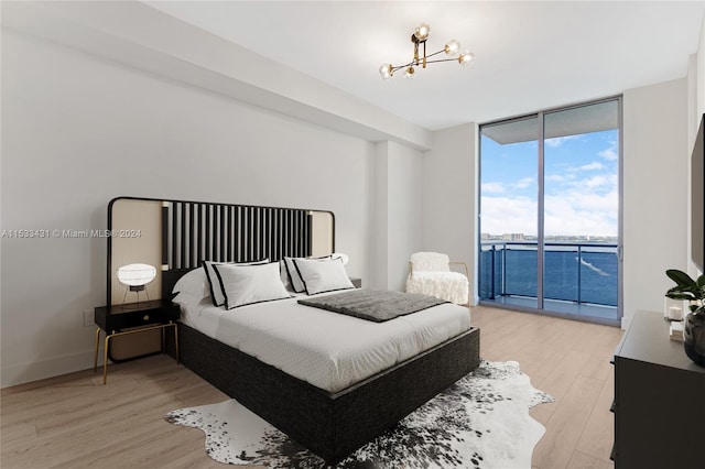 bedroom featuring an inviting chandelier, light hardwood / wood-style floors, a water view, access to outside, and floor to ceiling windows