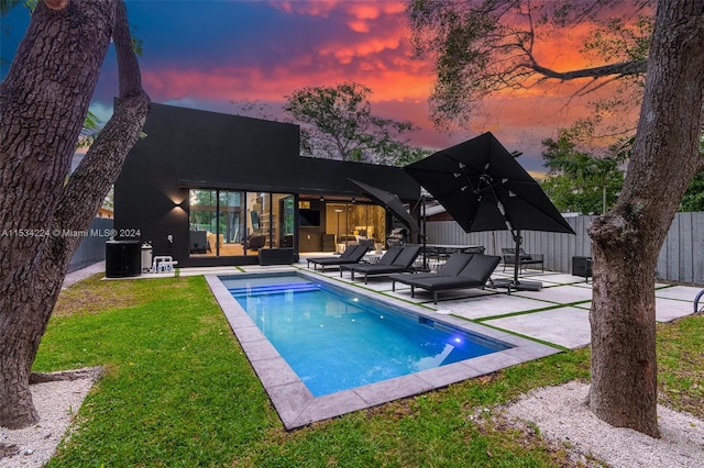 back house at dusk featuring a patio, central AC unit, a yard, a fenced in pool, and an outdoor living space