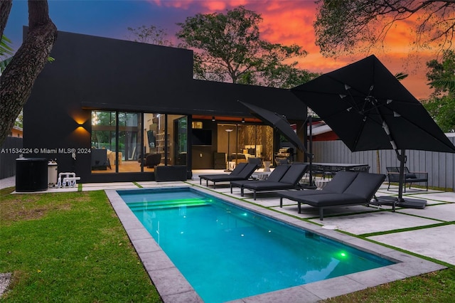 back house at dusk with an outdoor living space, a yard, and a patio