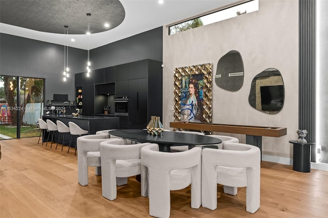 dining area with plenty of natural light, light hardwood / wood-style flooring, a towering ceiling, and sink