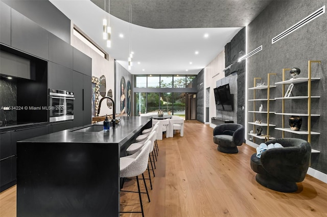 kitchen featuring a kitchen island with sink, hanging light fixtures, a breakfast bar, light hardwood / wood-style floors, and stainless steel oven