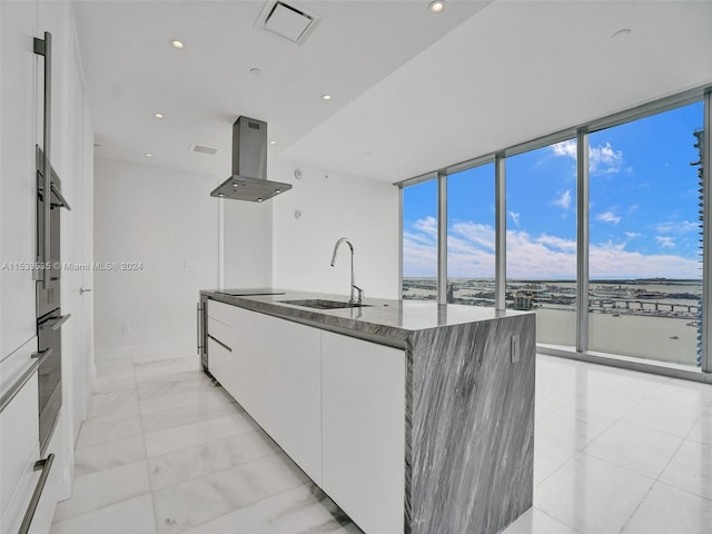 kitchen with sink, white cabinetry, light tile floors, and island range hood