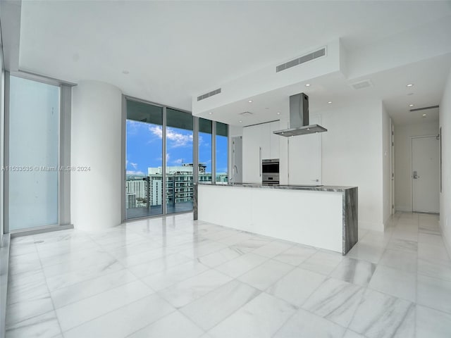 kitchen with a wall of windows, light tile floors, dark stone counters, white cabinets, and island range hood