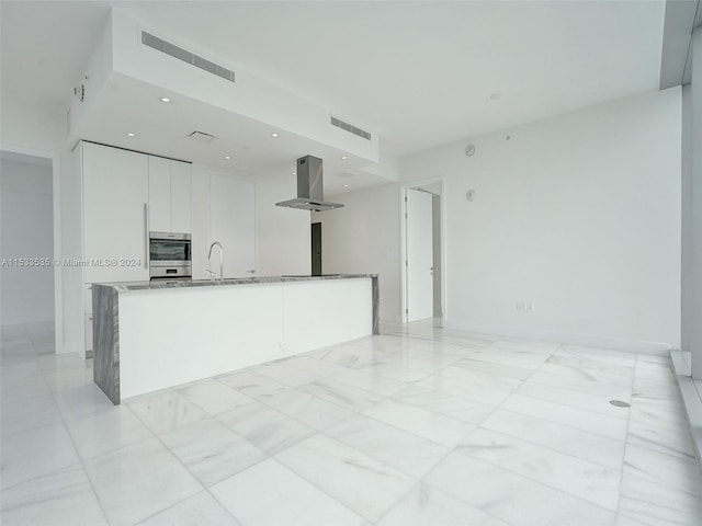 kitchen with a kitchen island with sink, island exhaust hood, stainless steel double oven, light tile flooring, and white cabinetry