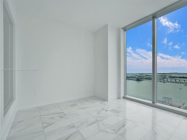 unfurnished room with expansive windows, light tile flooring, and a water view