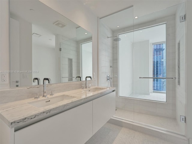 bathroom featuring a shower with shower door, large vanity, dual sinks, and a wealth of natural light