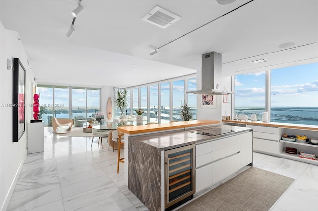 kitchen featuring wine cooler, island exhaust hood, white cabinetry, black electric stovetop, and a water view