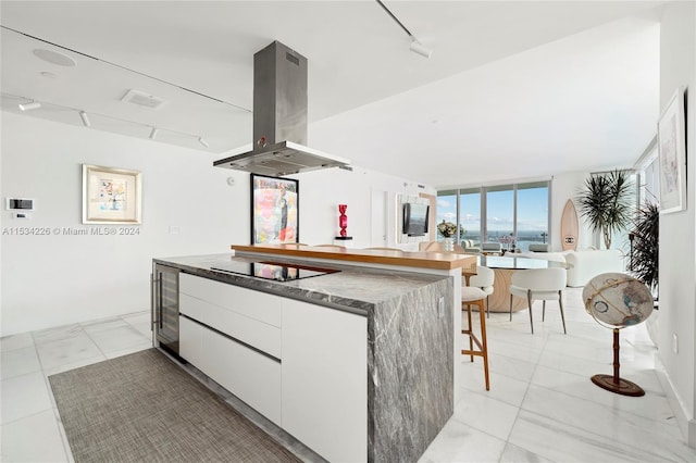 kitchen featuring island range hood, track lighting, white cabinetry, a kitchen breakfast bar, and black electric stovetop