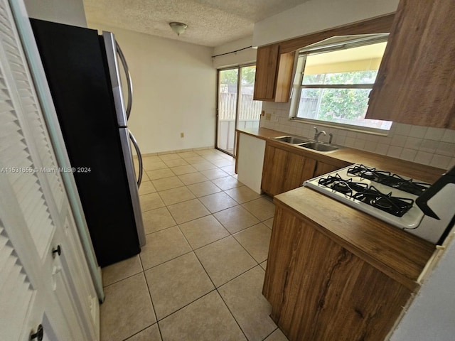 kitchen with sink, light tile floors, refrigerator, backsplash, and gas stovetop