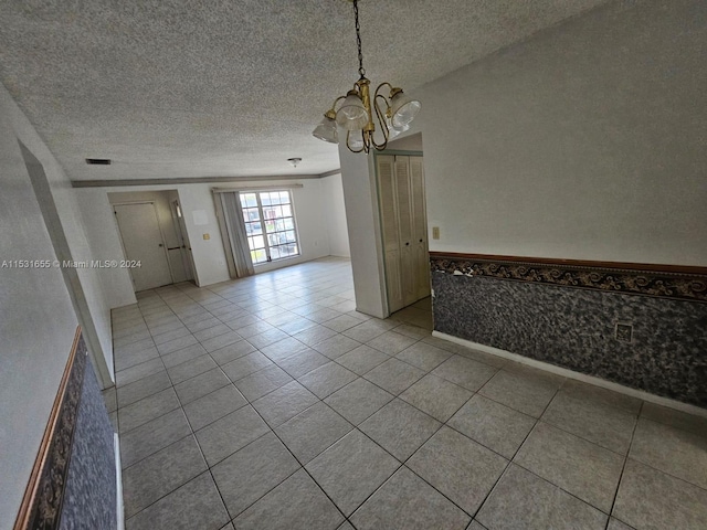 spare room featuring an inviting chandelier, a textured ceiling, and light tile flooring