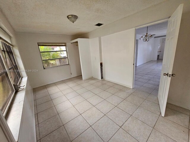 empty room with a chandelier, a textured ceiling, and light tile floors