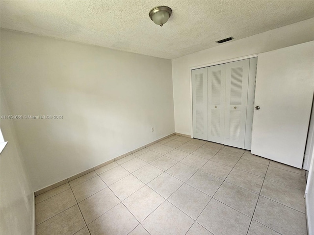 unfurnished bedroom featuring a closet, light tile floors, and a textured ceiling