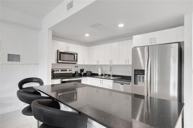 kitchen with appliances with stainless steel finishes, sink, light tile patterned floors, dark stone countertops, and white cabinetry