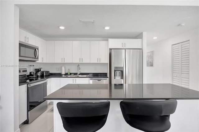 kitchen featuring sink, light tile patterned flooring, a breakfast bar area, white cabinets, and appliances with stainless steel finishes