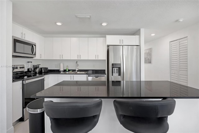 kitchen featuring dark stone counters, white cabinets, a kitchen breakfast bar, sink, and stainless steel appliances