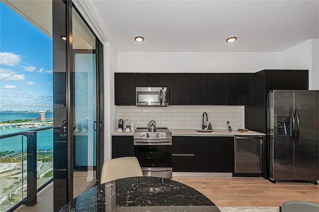 kitchen featuring backsplash, sink, light hardwood / wood-style flooring, a water view, and stainless steel appliances