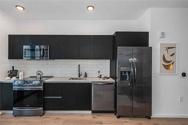 kitchen featuring backsplash, black appliances, sink, and light wood-type flooring