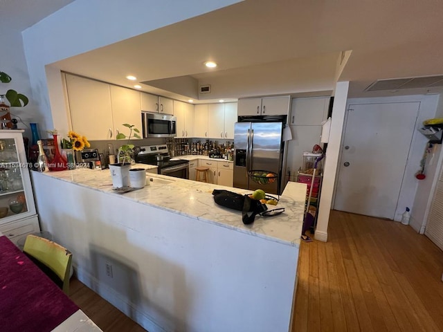 kitchen with backsplash, white cabinets, appliances with stainless steel finishes, and light wood-type flooring