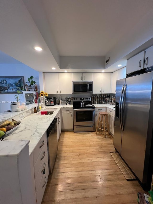 kitchen featuring appliances with stainless steel finishes, white cabinetry, sink, and light hardwood / wood-style flooring