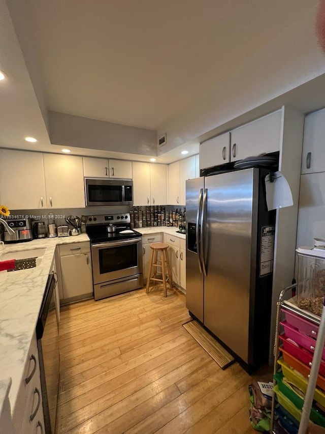 kitchen featuring backsplash, stainless steel appliances, white cabinets, and light wood-type flooring