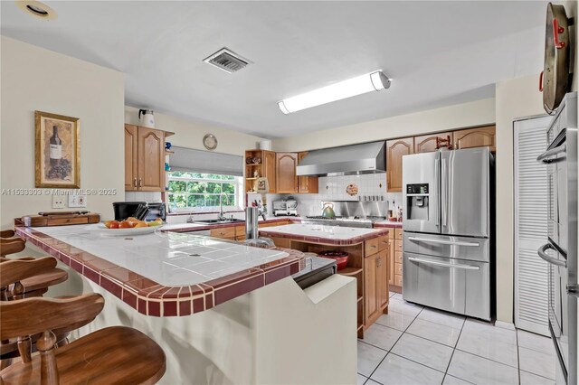 kitchen featuring light tile patterned floors, tile counters, a kitchen island, stainless steel appliances, and wall chimney range hood