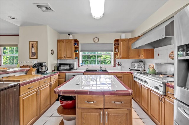 kitchen with tile countertops, sink, a center island, light tile patterned floors, and stainless steel appliances