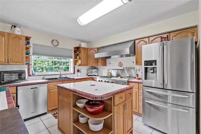 kitchen with wall chimney range hood, sink, light tile patterned floors, stainless steel appliances, and a center island