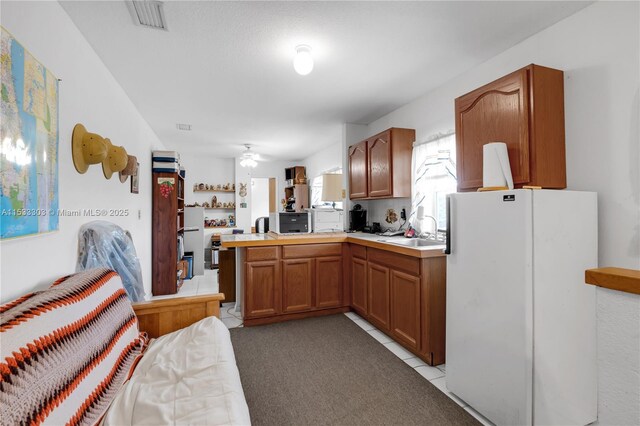 kitchen with light tile patterned flooring, sink, kitchen peninsula, white fridge, and ceiling fan