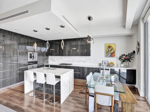 kitchen featuring light wood-type flooring, sink, pendant lighting, stainless steel gas stovetop, and a center island with sink