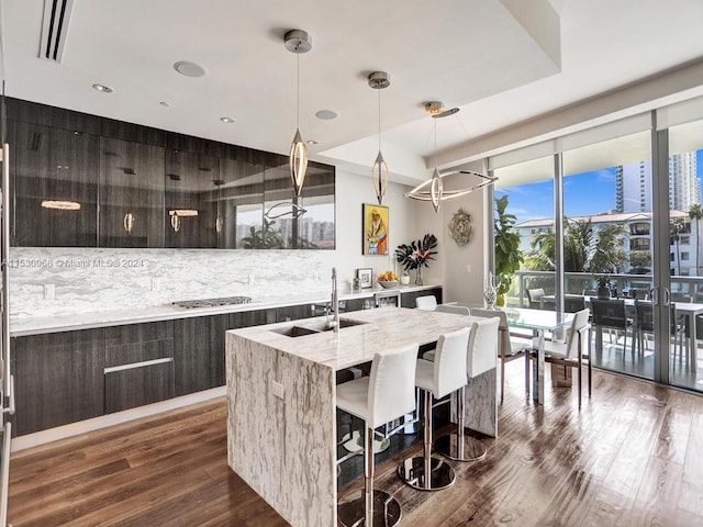 kitchen featuring dark wood-type flooring, a kitchen island with sink, sink, and decorative light fixtures