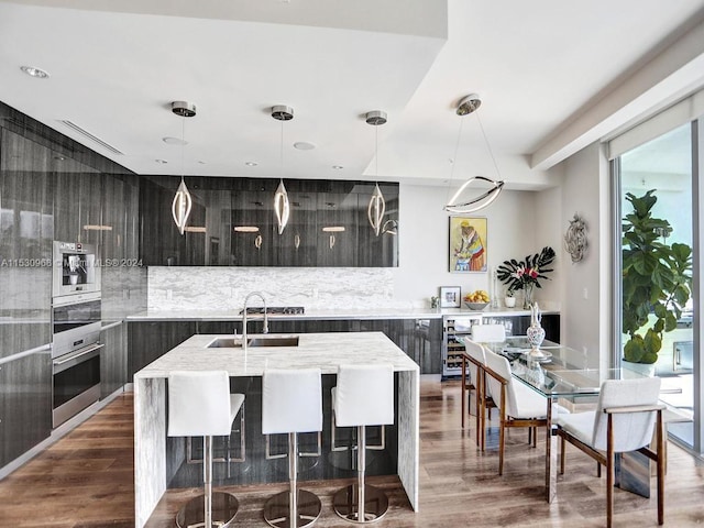 kitchen with pendant lighting, an island with sink, sink, backsplash, and dark hardwood / wood-style floors