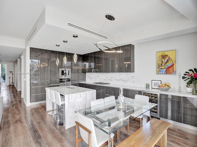 kitchen featuring an island with sink, tasteful backsplash, beverage cooler, light hardwood / wood-style flooring, and decorative light fixtures