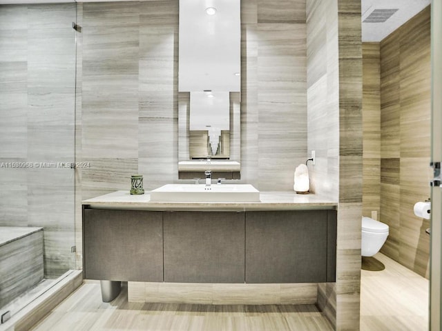 bathroom with walk in shower, tile walls, vanity, and toilet