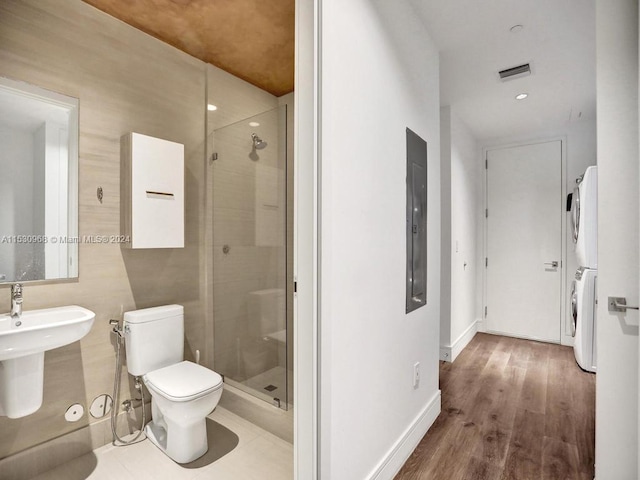 bathroom with hardwood / wood-style floors, a shower with door, electric panel, stacked washer / drying machine, and toilet