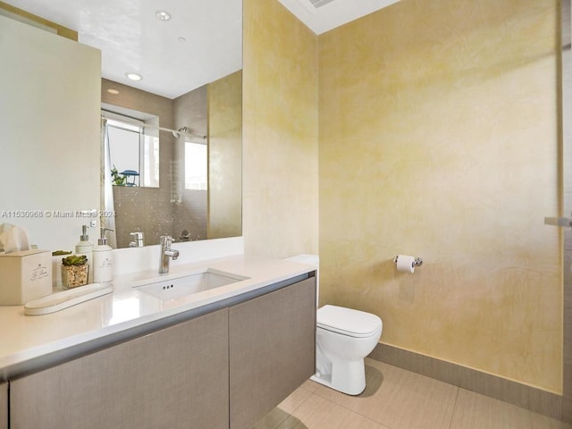 bathroom with tile patterned flooring, tiled shower, vanity, and toilet