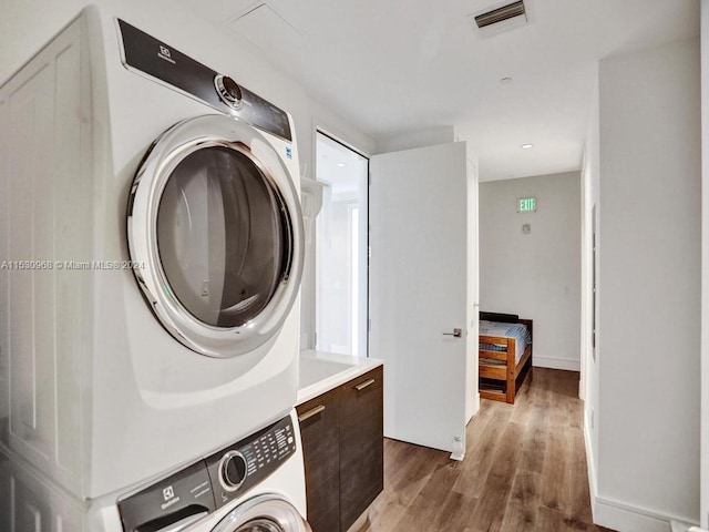 clothes washing area featuring hardwood / wood-style flooring and stacked washer / dryer