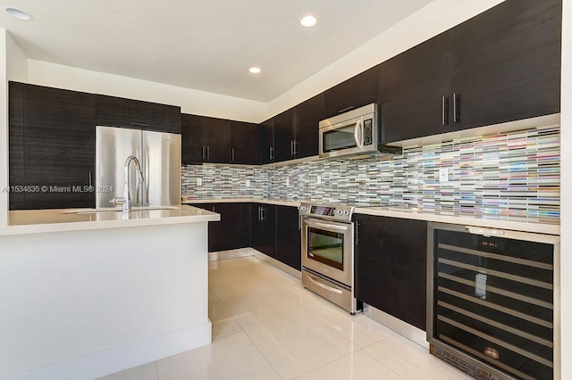 kitchen featuring light tile floors, beverage cooler, tasteful backsplash, dark brown cabinets, and appliances with stainless steel finishes