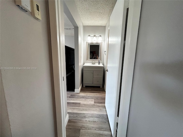 hall with a textured ceiling, sink, and light hardwood / wood-style flooring