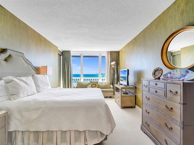 bedroom with light carpet, a textured ceiling, floor to ceiling windows, and a water view