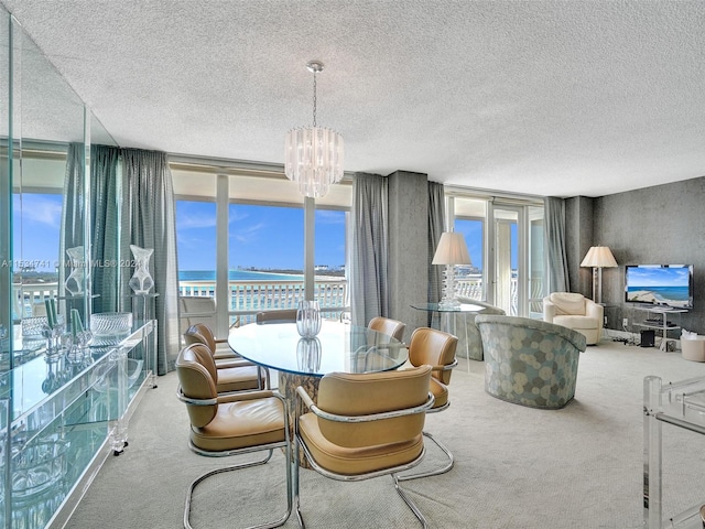 carpeted dining space featuring a water view, a wall of windows, a textured ceiling, and an inviting chandelier