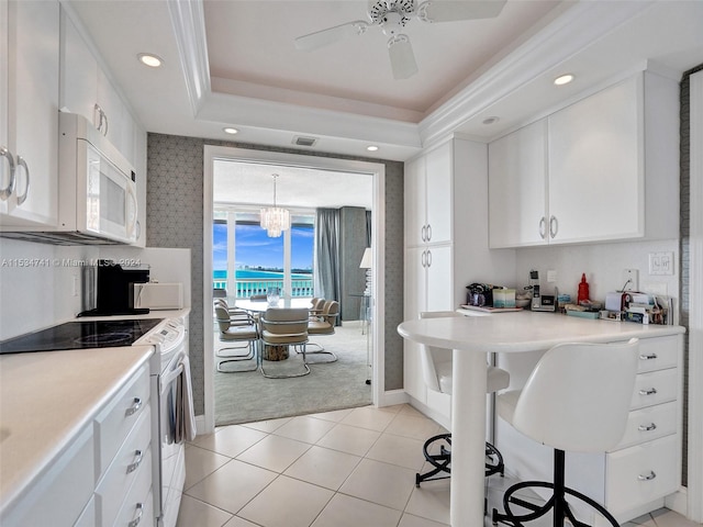 kitchen with light tile floors, a tray ceiling, white appliances, and white cabinetry