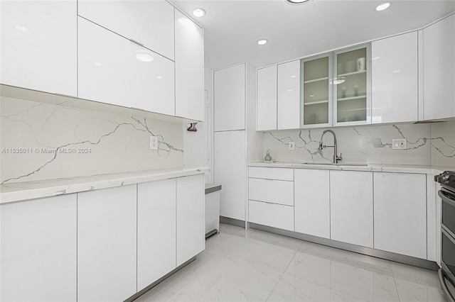 kitchen with light tile floors, stainless steel electric stove, tasteful backsplash, white cabinetry, and sink