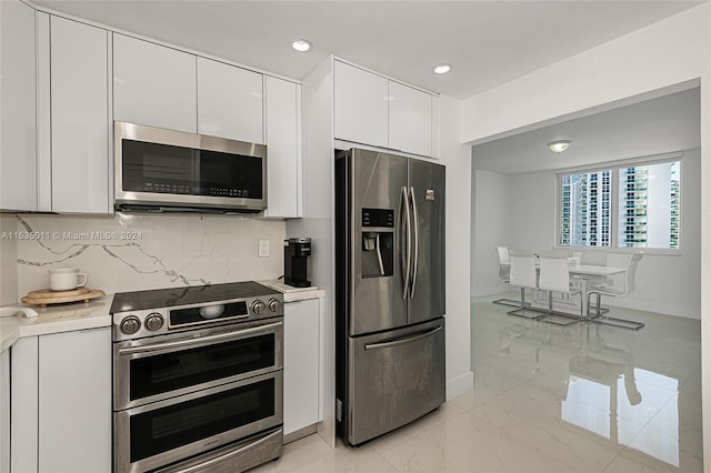 kitchen with backsplash, white cabinets, appliances with stainless steel finishes, and light tile floors