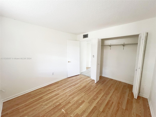 unfurnished bedroom with light wood-type flooring, a textured ceiling, and a closet